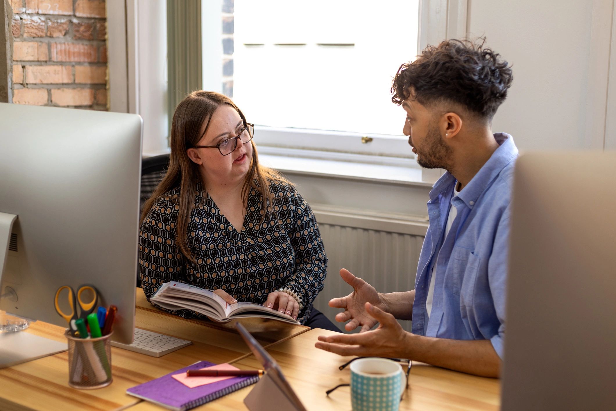 Two professionals in a coaching-style conversation at a desk